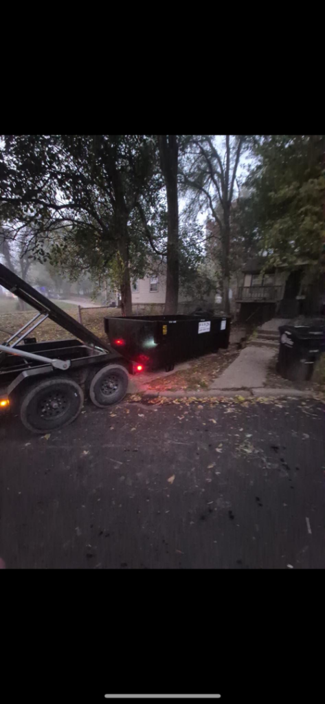 An H & H Dumpster Rental truck picking up an empty dumpster from a street at dusk in Rootstown, OH.