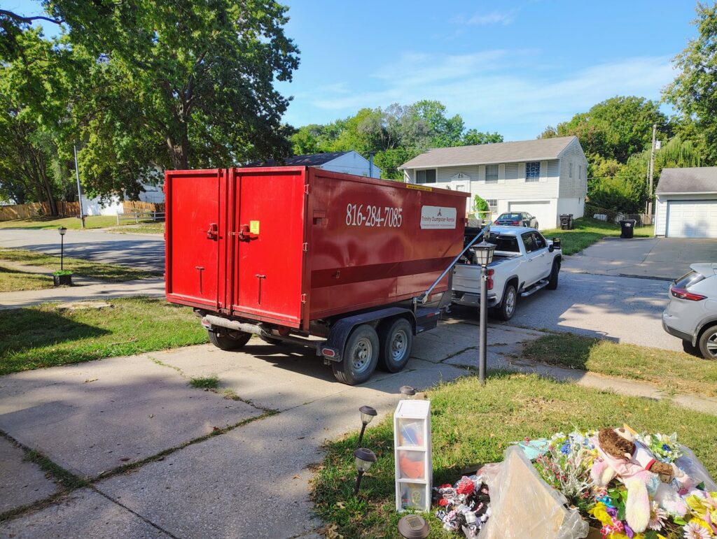 A red dumpster being picked up after a residential junk removal job by Trinity Dumpster Rental LLC in Kansas City, MO.