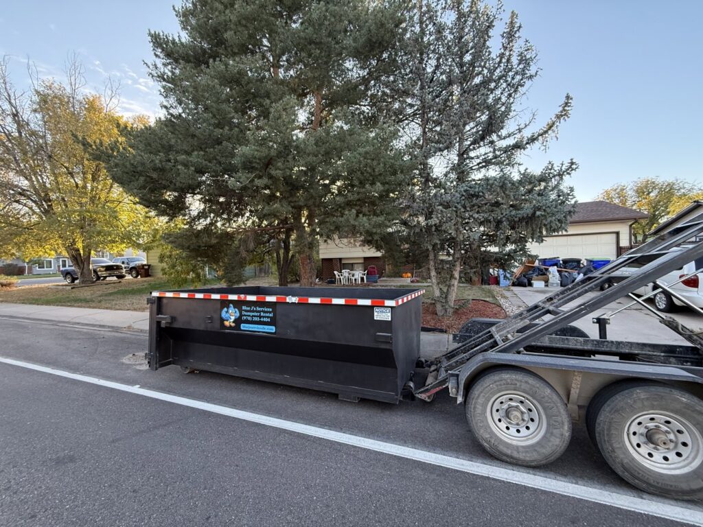 A Blue J's Services Dumpster Rental truck picking up an empty dumpster from a residential street in Greeley, CO.