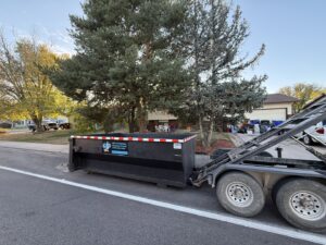 A Blue J's Services Dumpster Rental truck picking up an empty dumpster from a residential street in Greeley, CO.