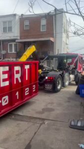 A Geppert Recycling truck picking up a red dumpster from a residential street for junk removal in Philadelphia, PA.
