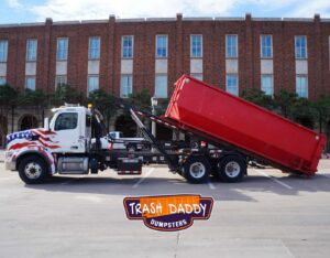 A Trash Daddy truck with an American flag design picking up a red dumpster in Fort Worth, TX