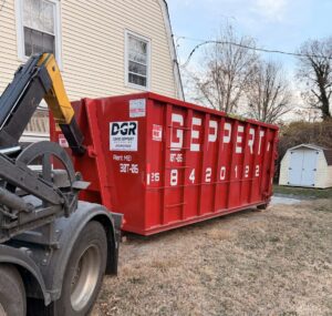 A Geppert Recycling truck placing a large red dumpster in a backyard for junk removal services in Philadelphia, PA.