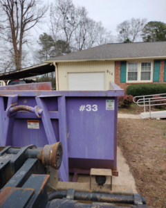 An All In Waste dumpster being placed next to a residential house in Greenville, SC.