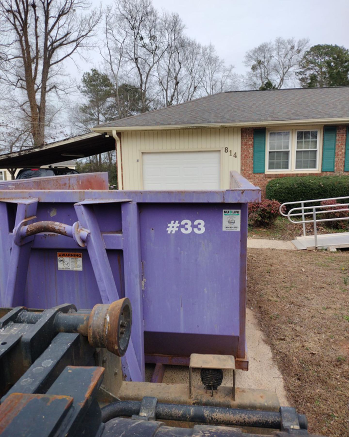 An All In Waste dumpster being placed next to a residential house in Greenville, SC.