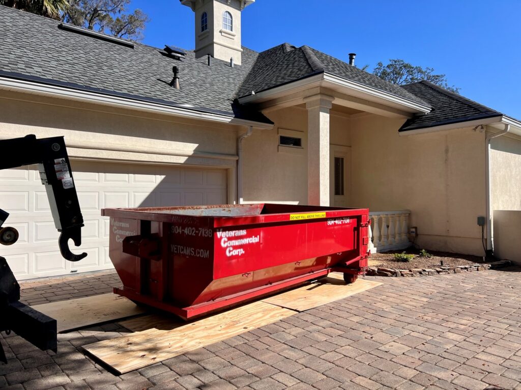 A red dumpster from Vetcans Dumpster Rental being carefully placed on wooden planks in a residential driveway in Jacksonville, FL.