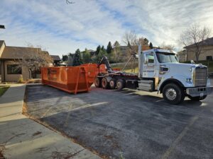 A Rushmore Dumpster truck placing an orange roll-off dumpster in a parking lot for a job in Rapid City, SD.