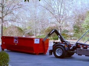 A Waste Removal USA truck placing or picking up a red roll-off dumpster in a parking lot for junk removal in Austin, TX