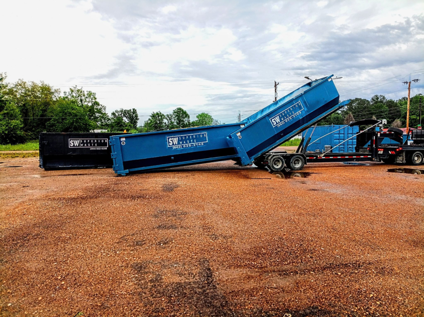 A blue dumpster being placed or picked up by a truck for junk removal service by Superior Waste Management in Amory, MS.