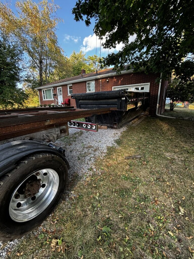 A roll-off truck placing or picking up a black dumpster next to a house for junk removal by Wagners Property Services LLC in Canton, OH.