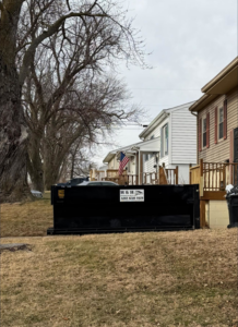 An H & H Dumpster Rental dumpster placed on a lawn in front of residential homes in Rootstown, OH.