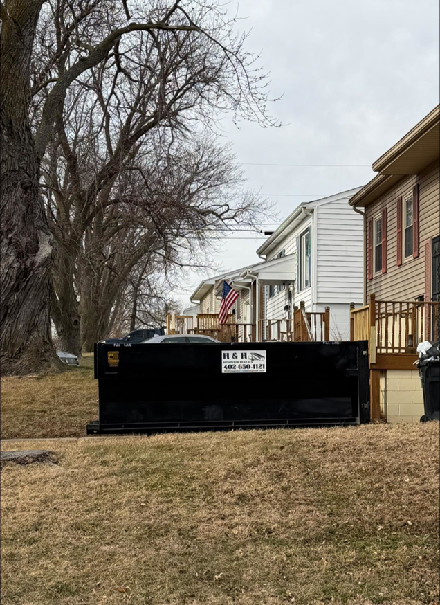 An H & H Dumpster Rental dumpster placed on a lawn in front of residential homes in Rootstown, OH.