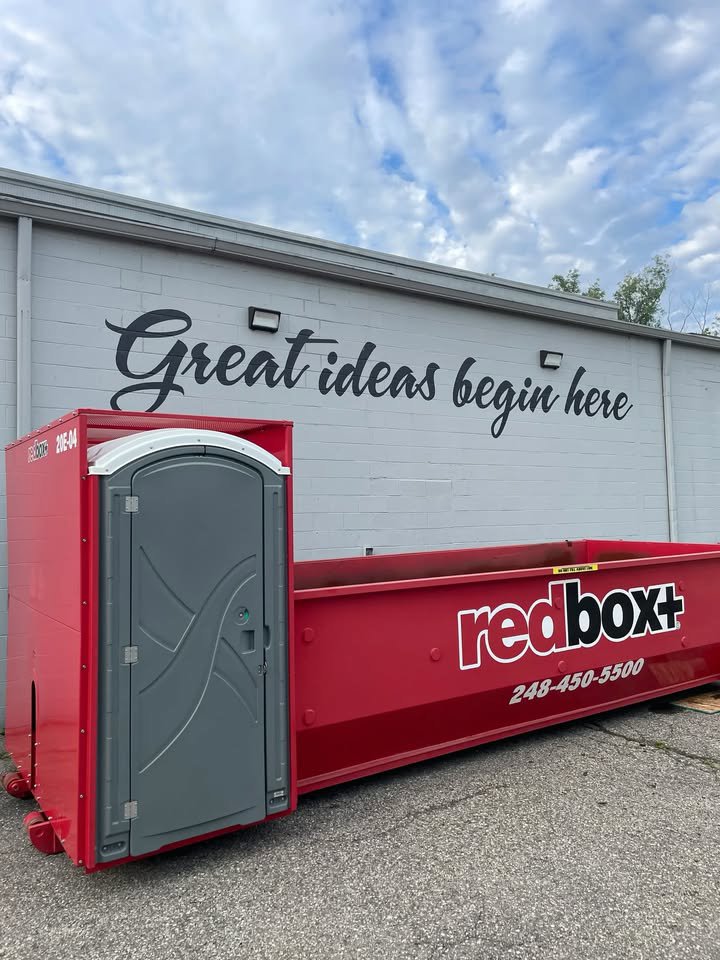 A redbox+ dumpster with a portable toilet at a commercial building for redbox+ Dumpsters of Greater Austin in Austin, TX