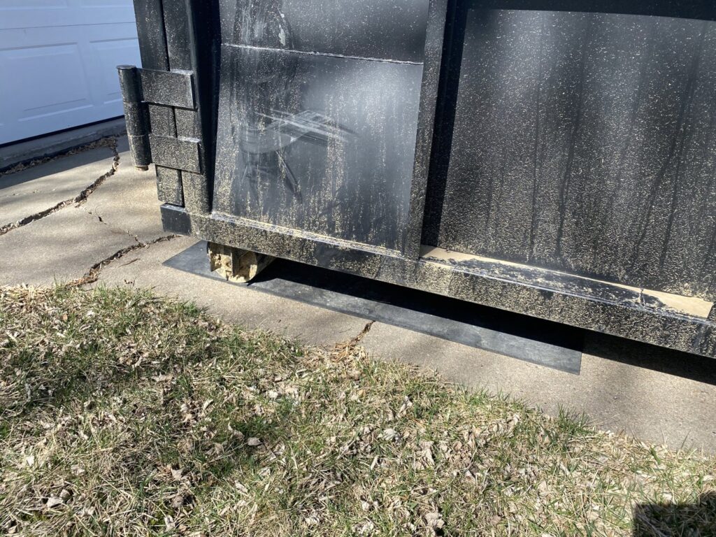 Protective boards placed under a 402 Container dumpster on a driveway for junk removal in Omaha, NE.