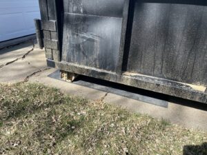 Protective boards placed under a 402 Container dumpster on a driveway for junk removal in Omaha, NE.