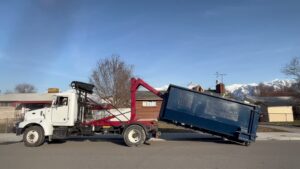 A truck removing a blue dumpster from a street, demonstrating the junk removal service of Blue Bin Dumpster Rentals in Salt Lake City, UT.