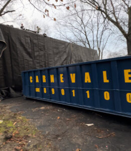 An AJ Carnevale Disposal dumpster positioned at a renovation site with workers on the roof in Hamilton, NJ