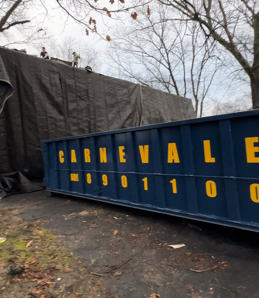 An AJ Carnevale Disposal dumpster positioned at a renovation site with workers on the roof in Hamilton, NJ