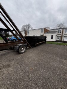 A black roll-off dumpster being delivered or picked up at an apartment complex by Wagners Property Services LLC for junk removal in Canton, OH.