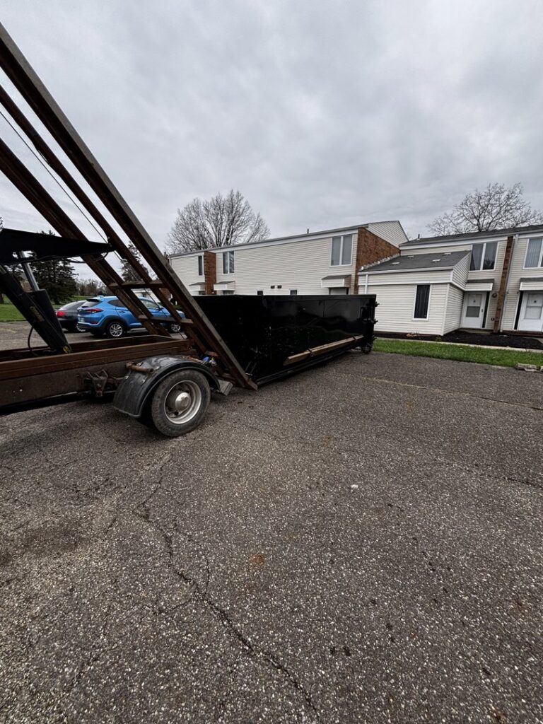 A black roll-off dumpster being delivered or picked up at an apartment complex by Wagners Property Services LLC for junk removal in Canton, OH.