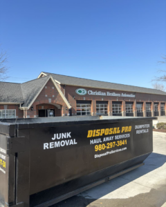 A branded dumpster from Disposal Pro Haul Away Services for junk removal and dumpster rentals, parked outside an automotive shop in Charlotte, NC.