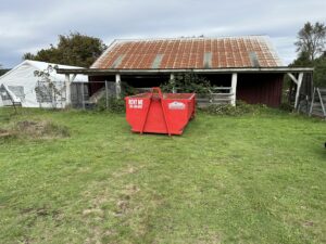 A red dumpster from Cascade Container and Recycling with a 'Rent Me' sign next to an old barn in Seattle, WA.
