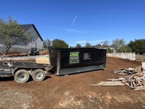 A G.I. HAUL Austin, TX branded dumpster on a trailer, positioned next to a pile of wood debris at a construction site.