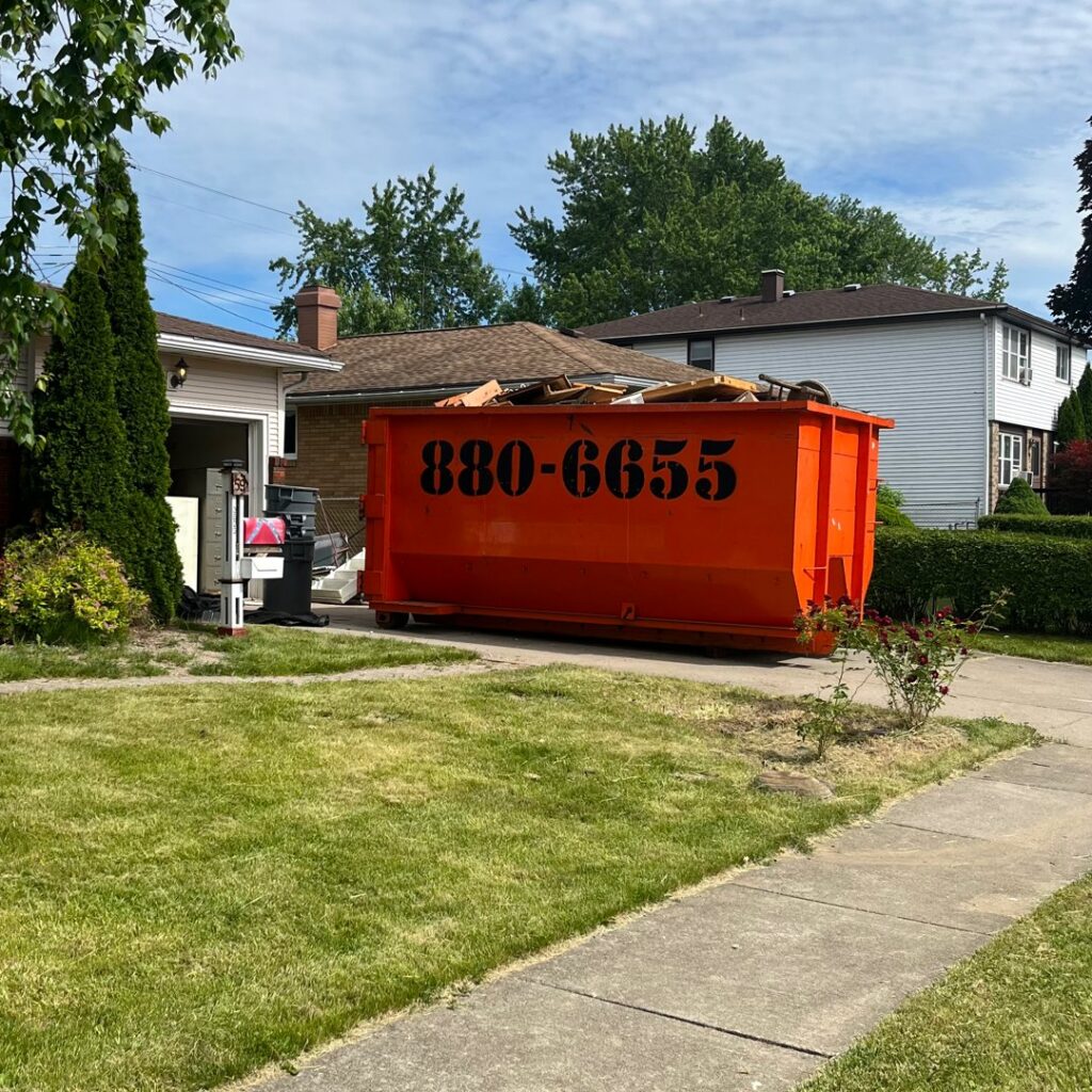 An orange dumpster rental filled with construction debris in a residential driveway from Frankie's Removal Services & Dumpster Rental in Buffalo, NY