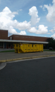 A yellow Elite Waste Services dumpster placed for junk removal at Charles E Jordan Senior High School in Raleigh, NC.