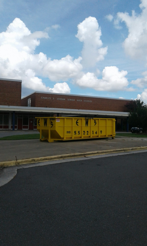 A yellow Elite Waste Services dumpster placed for junk removal at Charles E Jordan Senior High School in Raleigh, NC.