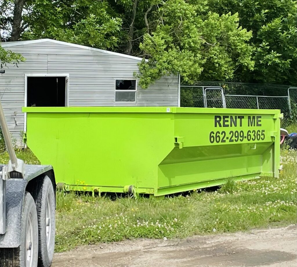 A bright green dumpster placed next to a shed for junk removal services by Tristate Dumpsters LLC in Greenville, MS.