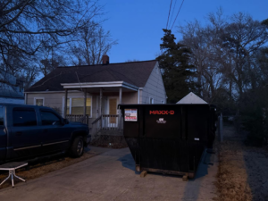 A black dumpster from Great Bridge Bins, LLC placed in a residential driveway next to a pickup truck in Chesapeake, VA.
