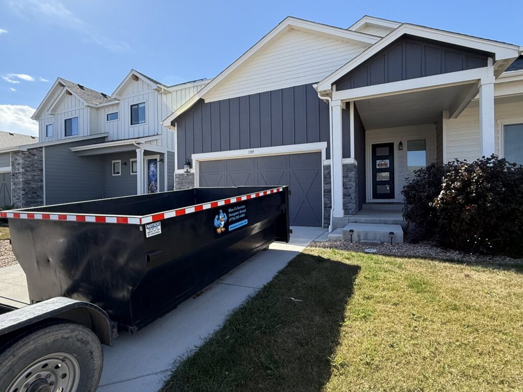 A black dumpster from Blue J's Services Dumpster Rental parked in a residential driveway in Greeley, CO, ready for junk removal.