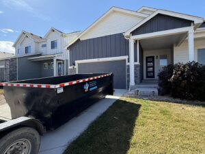 A black dumpster from Blue J's Services Dumpster Rental parked in a residential driveway in Greeley, CO, ready for junk removal.