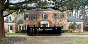 A large black dumpster from Parish Dumpsters, LLC placed in front of a residential home in Baton Rouge, LA.