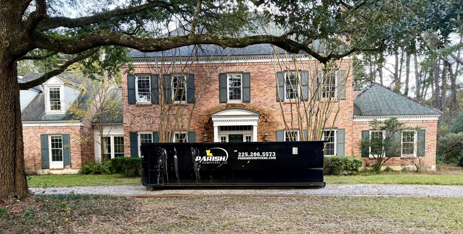 A large black dumpster from Parish Dumpsters, LLC placed in front of a residential home in Baton Rouge, LA.