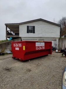 A red dumpster from Trinity Dumpster Rental LLC ready for use at a residential property in Kansas City, MO.