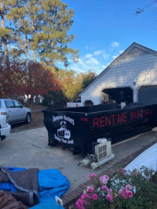 A black dumpster from Dumpster Busters parked in a driveway for junk removal service in Salemburg, NC.