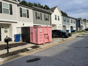A pink dumpster from Little Junkers placed on a street in front of townhouses for junk removal in Peachtree City, GA.
