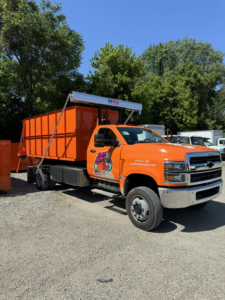 A bright orange Crazy Larry's Dumpster Rental truck with a dumpster loaded, ready for service in Columbus, OH.