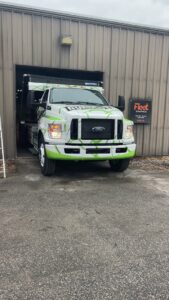 A Dump-It Dumpster Rentals truck, branded in green and white, exiting a garage in Concord, NH.