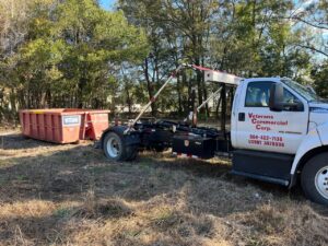 A Vetcans Dumpster Rental truck with a red dumpster in a grassy, undeveloped area in Jacksonville, FL.