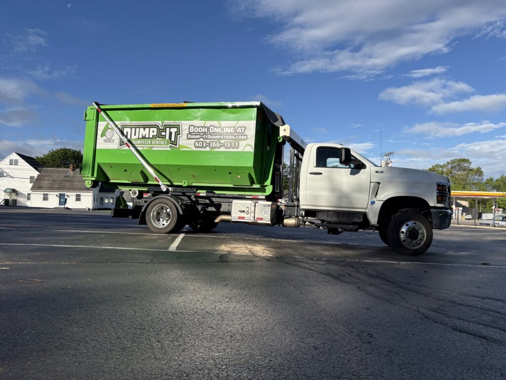 A Dump-It Dumpster Rentals truck with a green dumpster on its back, parked in a lot in Concord, NH.