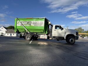 A Dump-It Dumpster Rentals truck with a green dumpster on its back, parked in a lot in Concord, NH.