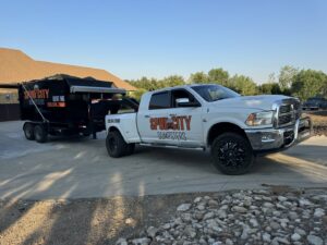 A SpudCity Dumpsters truck with a dumpster trailer parked on a driveway in Caldwell, ID.