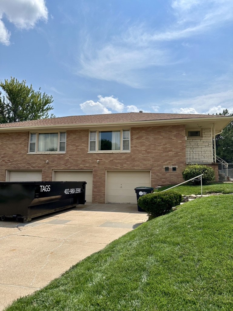 A black Tags Dumpsters roll-off dumpster placed in a residential driveway for home cleanout in Omaha, NE.