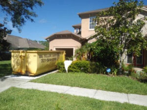 A Big Yellow Dumpster placed in front of a residential garage, suggesting a home renovation project by a general contractor in Saint Petersburg, FL.