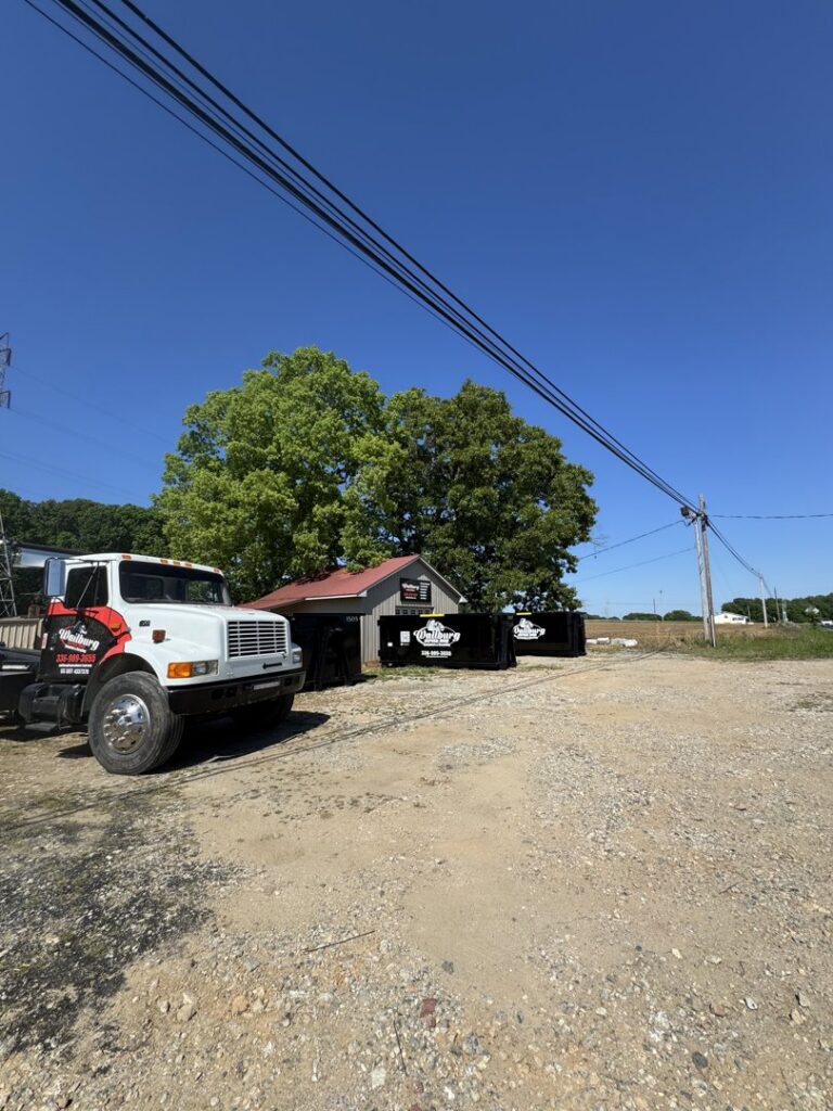 A Wallburg Disposal Worx LLC truck with a black dumpster parked near a building in High Point, NC.