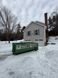 A green Dump-It Dumpster Rentals dumpster placed in a snowy residential driveway in Concord, NH.