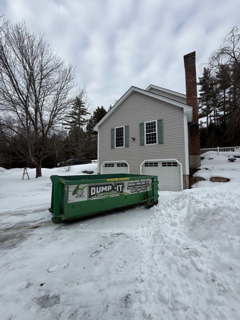 A green Dump-It Dumpster Rentals dumpster placed in a snowy residential driveway in Concord, NH.